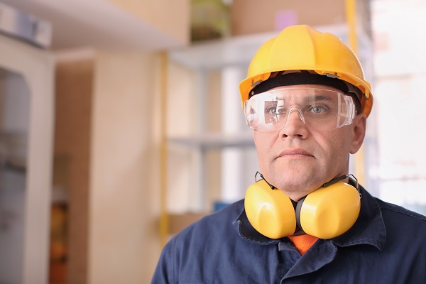 Male construction worker wearing a yellow hard hat, safety goggles, and ear protection, symbolizing workplace safety and the use of personal protective equipment (PPE).