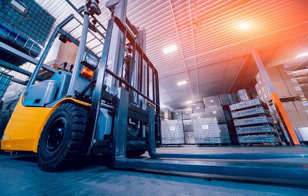 Low-angle view of a forklift in a warehouse filled with stacked pallets and boxes.