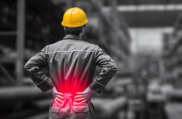 Construction worker wearing a yellow hard hat holding his lower back in pain, with a red highlight indicating injury.